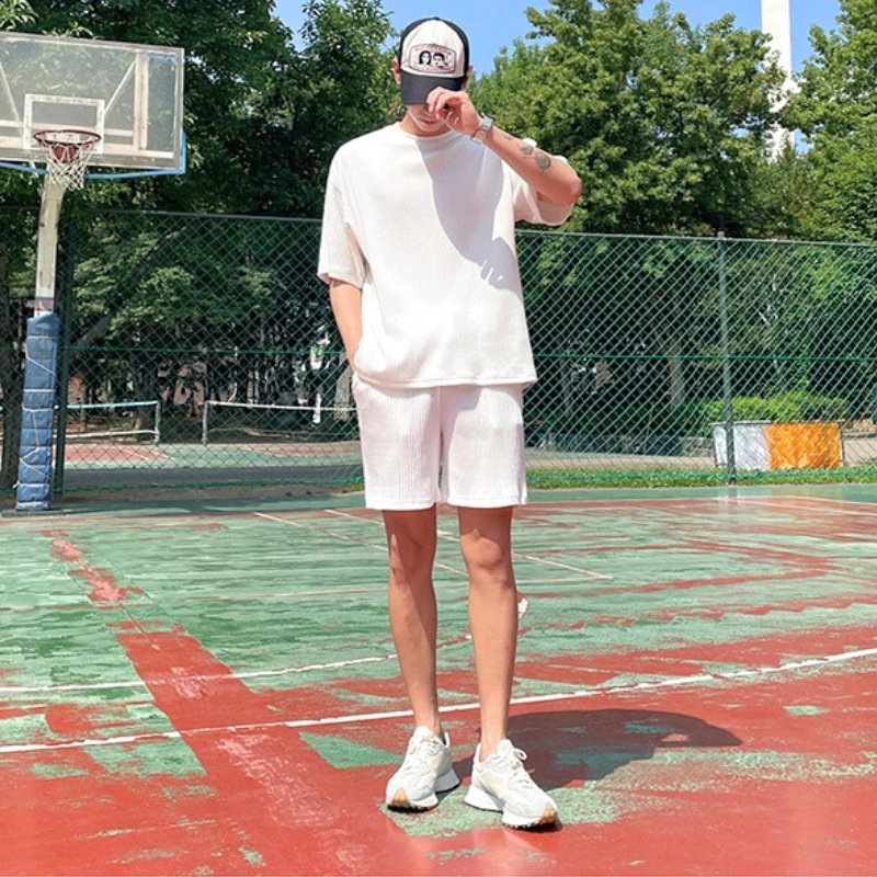 白のプリーツトップスとショートパンツをスタイリッシュに着こなす男性