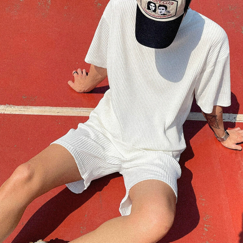 赤いバスケットコート上で座って白のプリーツショートセットアップを着る男性