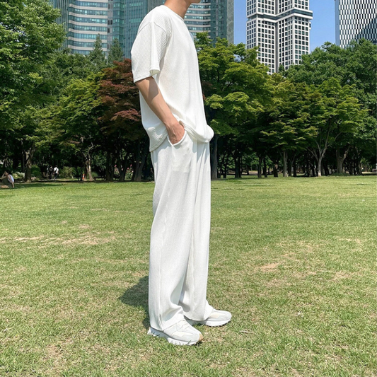 白のプリーツセットアップで立ち姿を見せる男性（横向き）